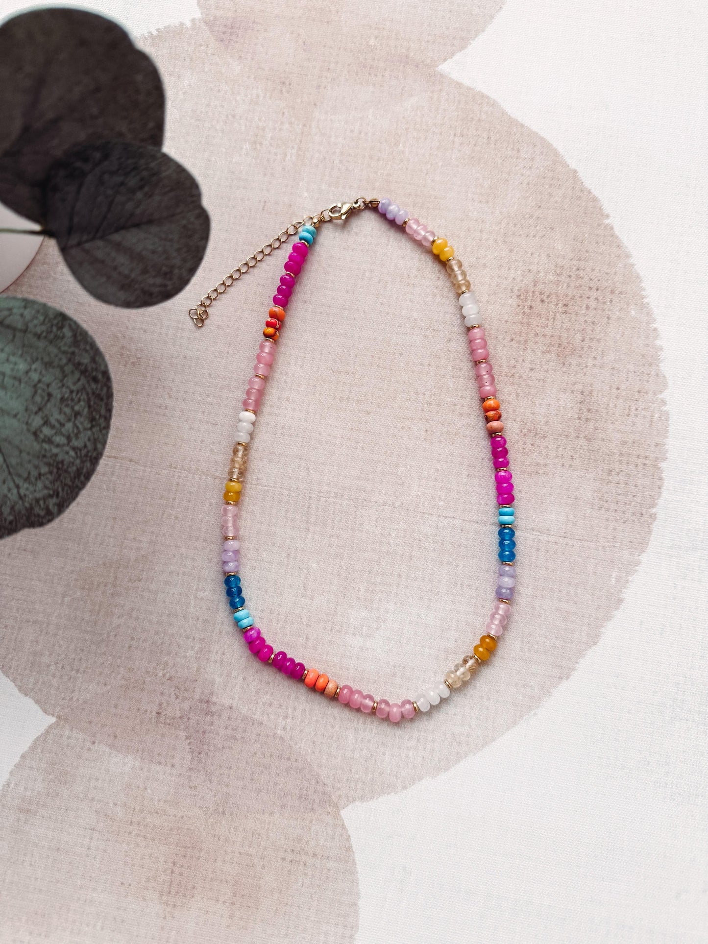 Colorful beaded necklace on a textured surface with floral elements