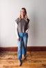 Woman wearing a sleeveless knitted top and blue jeans standing on a wooden floor.