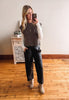 Woman taking a mirror selfie wearing a brown sweater vest, white shirt, black pants, and beige boots in a room with wooden flooring.