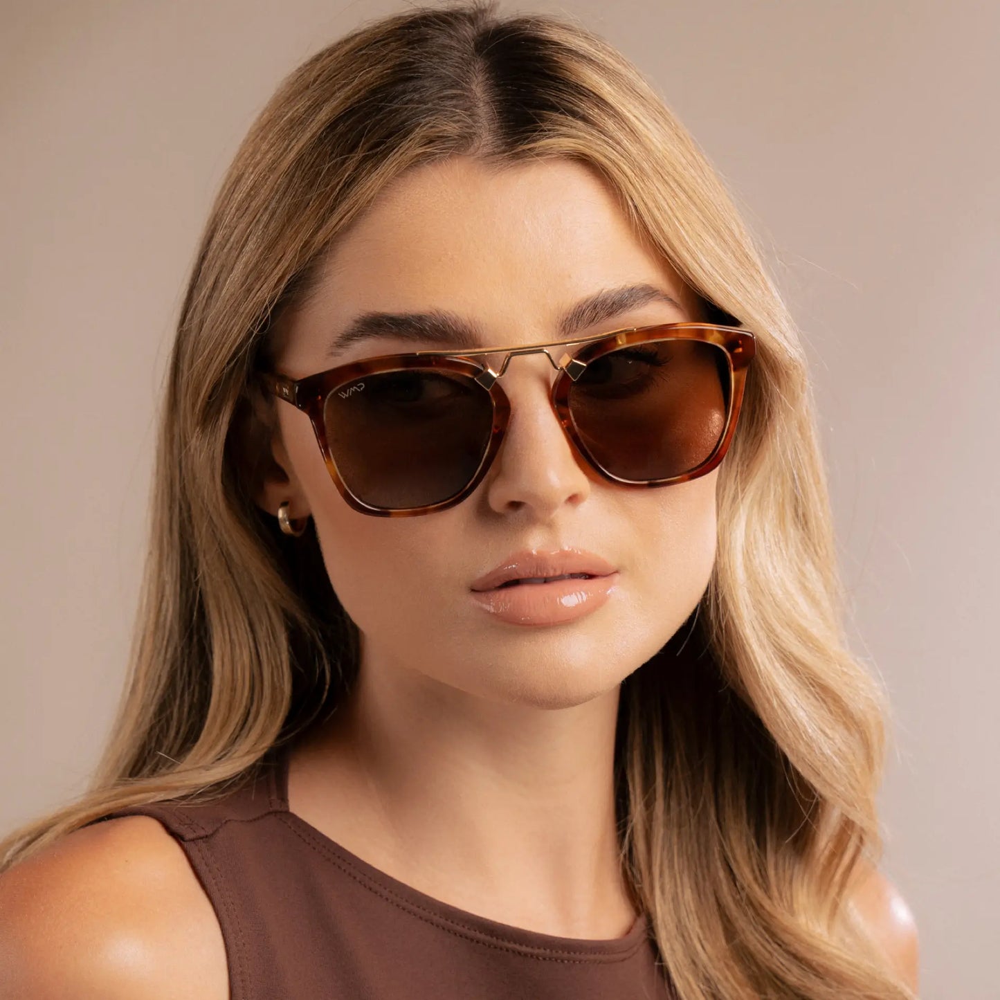 Woman wearing brown sunglasses with a neutral background