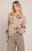 Woman wearing a beige sweater with black floral patterns on a plain background