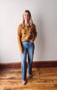 Woman wearing a mustard yellow cardigan and blue jeans standing on a wooden floor.
