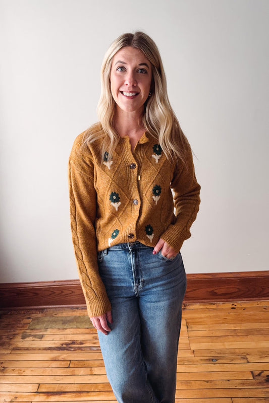 Woman wearing a mustard yellow cardigan with black buttons against a white wall.