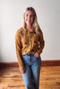 Woman wearing a mustard yellow cardigan with black buttons against a white wall.