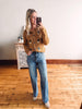 Woman taking a mirror selfie wearing a brown cardigan with colorful buttons and blue jeans.