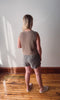 Person wearing a sleeveless brown top and striped shorts standing in a room with wooden flooring and white walls.