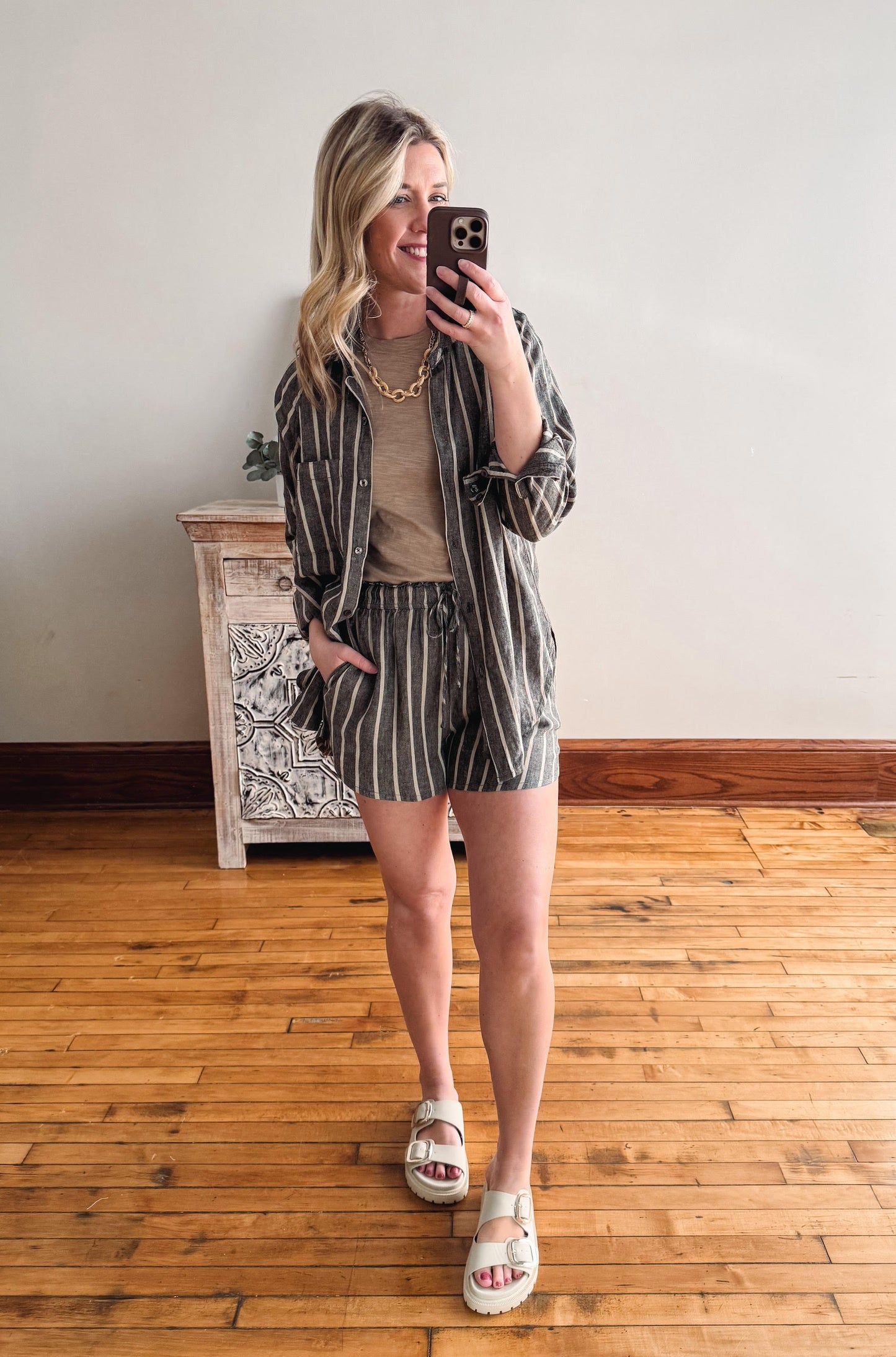 Woman taking a mirror selfie wearing a striped outfit in a room with wooden flooring.