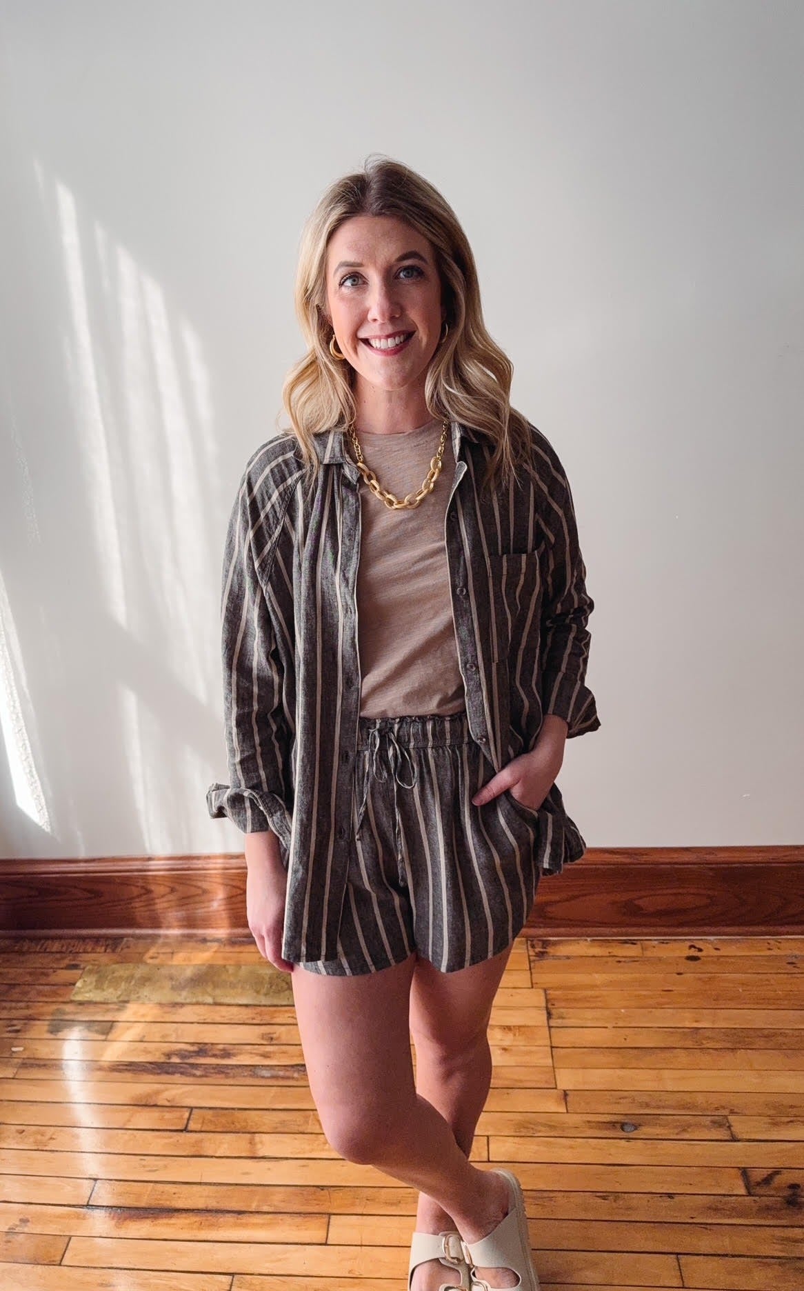 Woman wearing a striped shirt and shorts standing on a wooden floor.