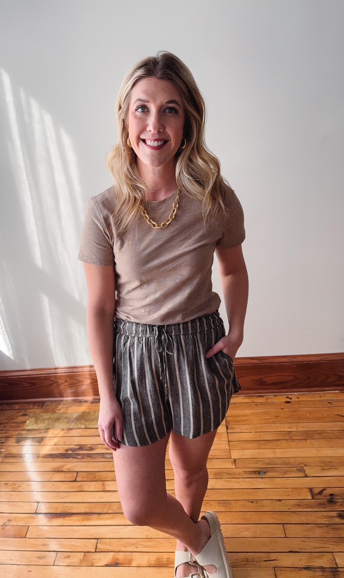 Woman wearing a beige t-shirt and striped shorts standing on a wooden floor.