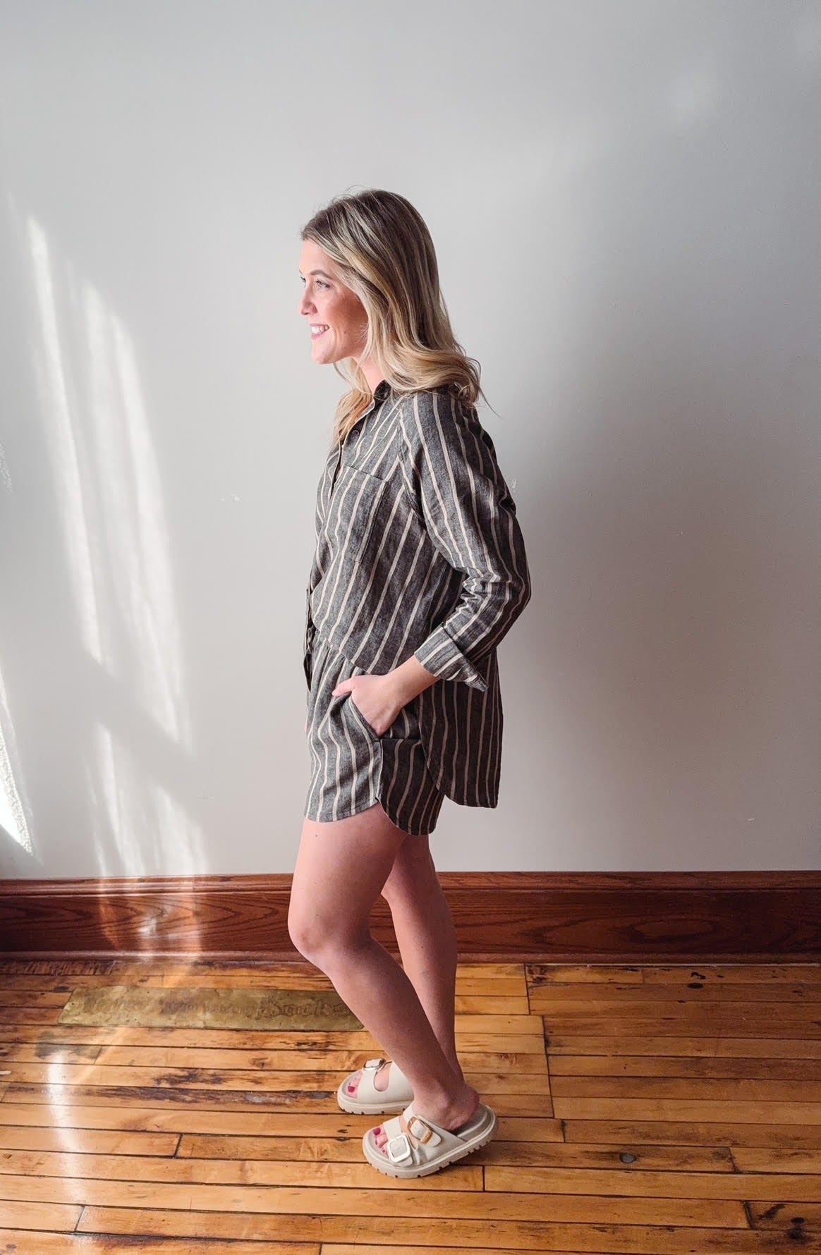 Woman wearing a striped dress standing on a wooden floor with a white wall background