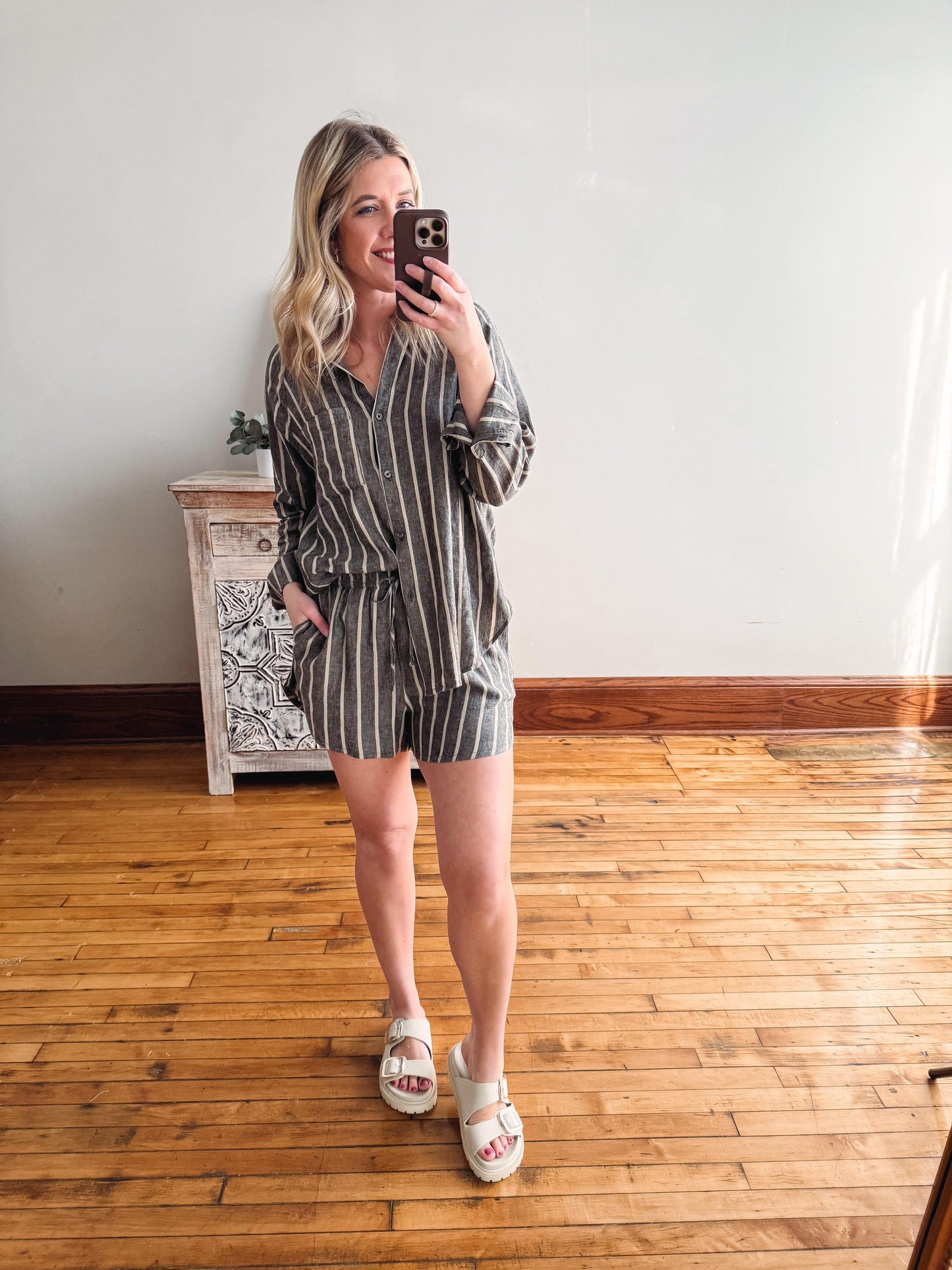 Woman taking a mirror selfie wearing a striped romper in a room with wooden flooring.
