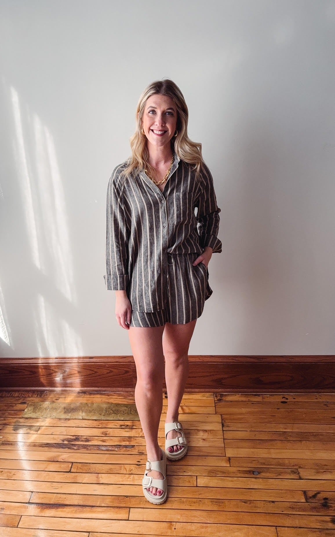 Woman standing on a wooden floor wearing a striped dress and sandals.