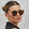 Woman wearing brown sunglasses with a neutral background