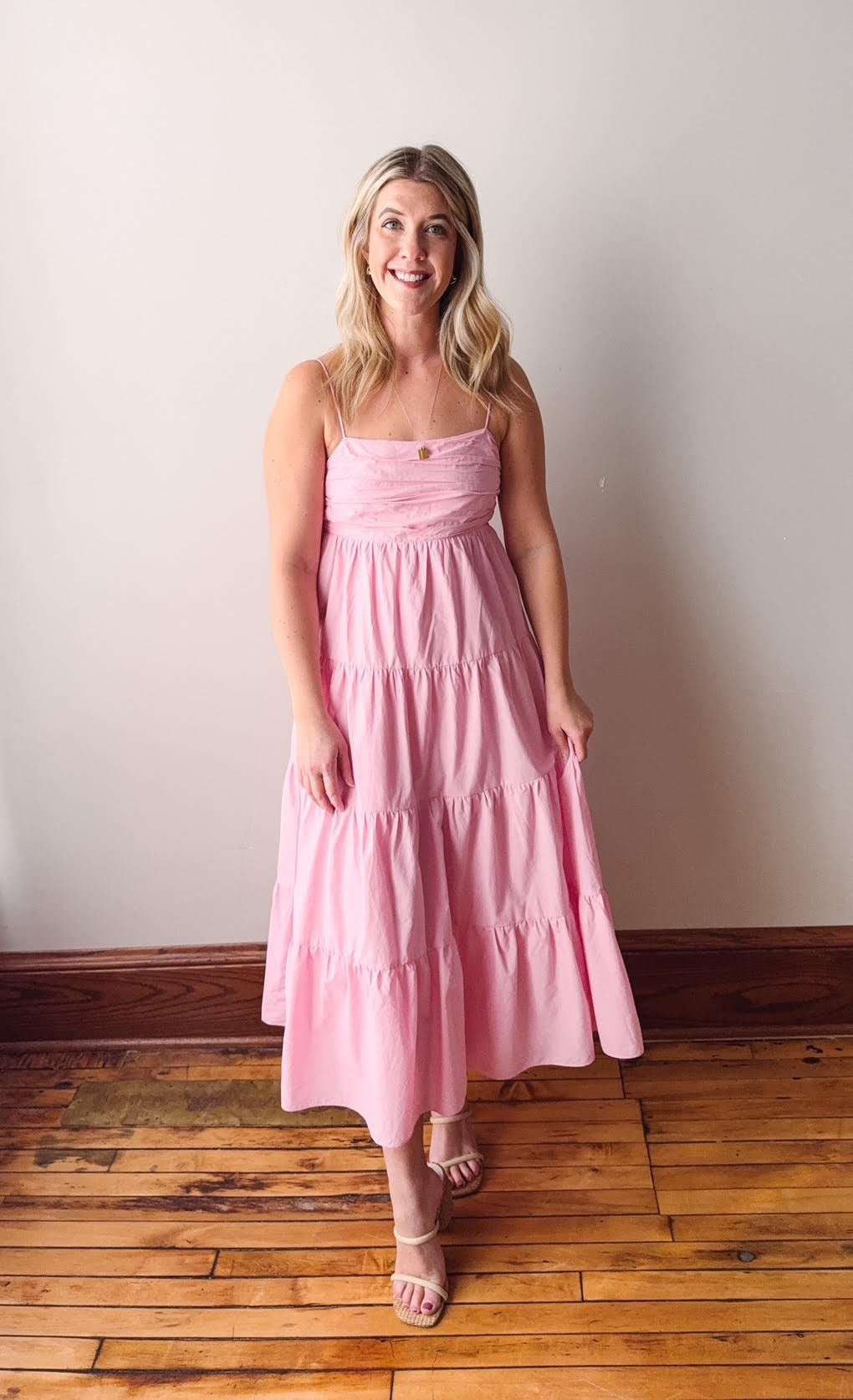 Woman wearing a pink dress standing on a wooden floor against a white wall