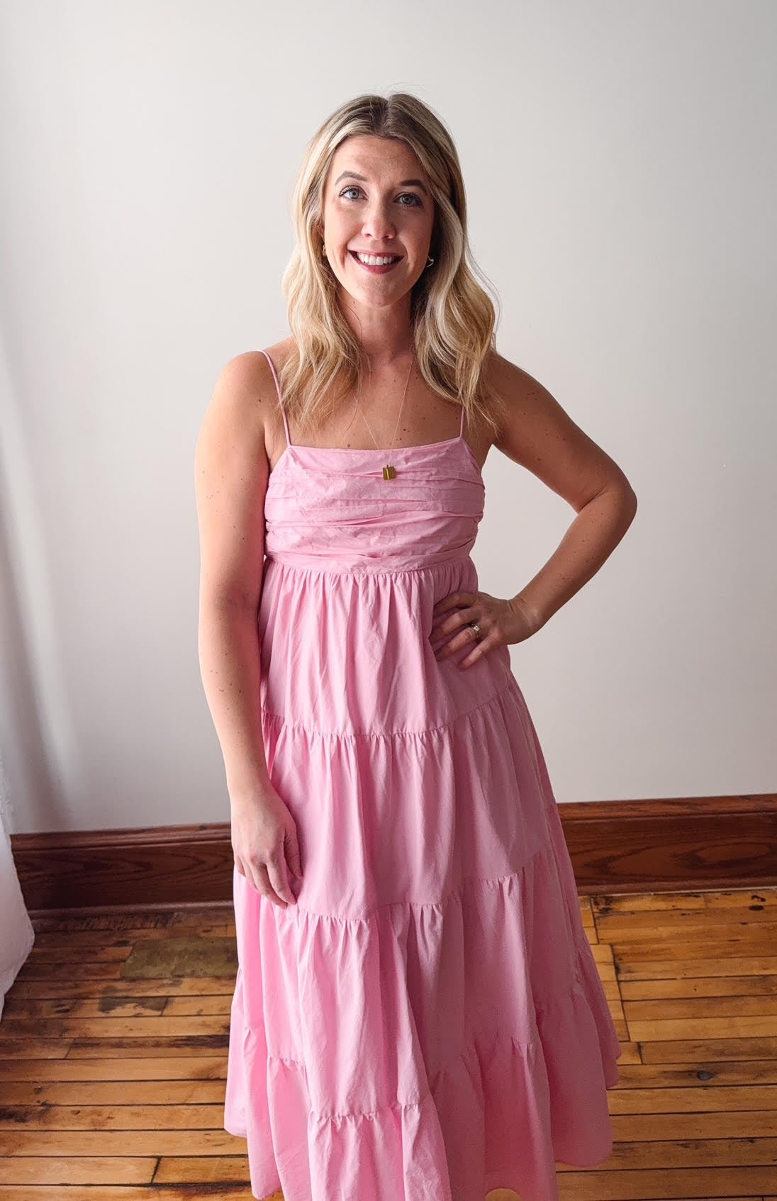 Woman wearing a pink dress standing against a white wall.