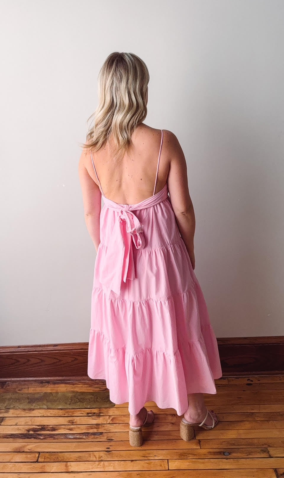 Woman wearing a pink dress with a white wall and wooden floor background