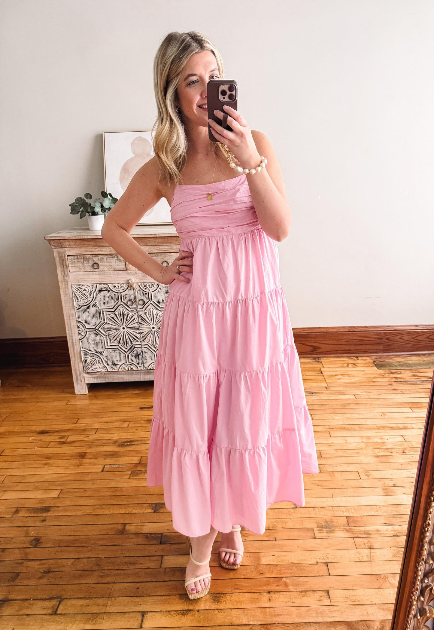 Woman in a pink dress taking a mirror selfie in a room with wooden flooring.