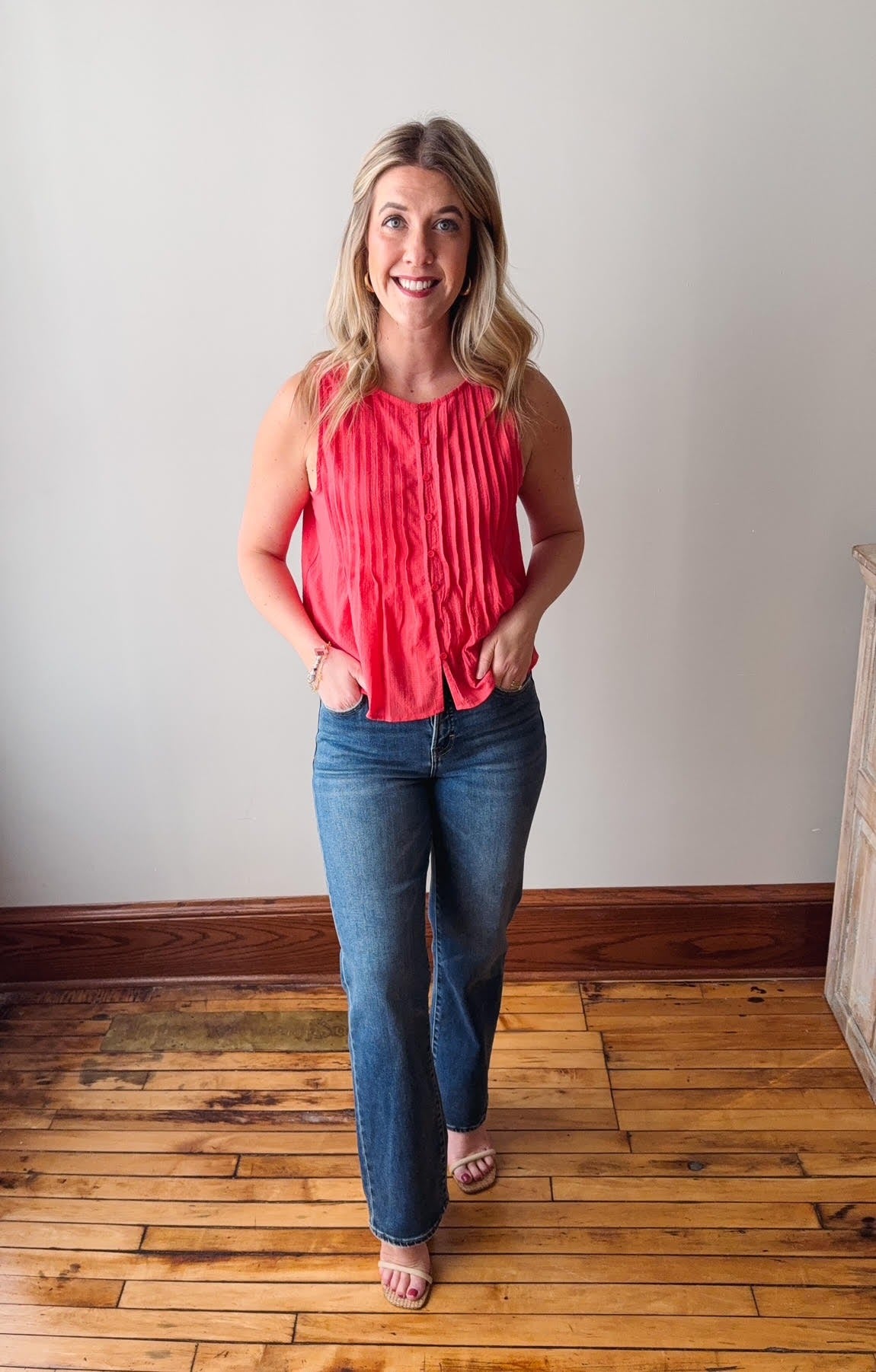 Woman wearing a coral top and blue jeans standing on a wooden floor.