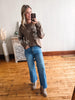 Woman taking a mirror selfie wearing a brown sweater with white floral patterns and blue jeans.