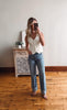 Woman taking a mirror selfie wearing a white blouse and blue jeans in a room with wooden flooring.