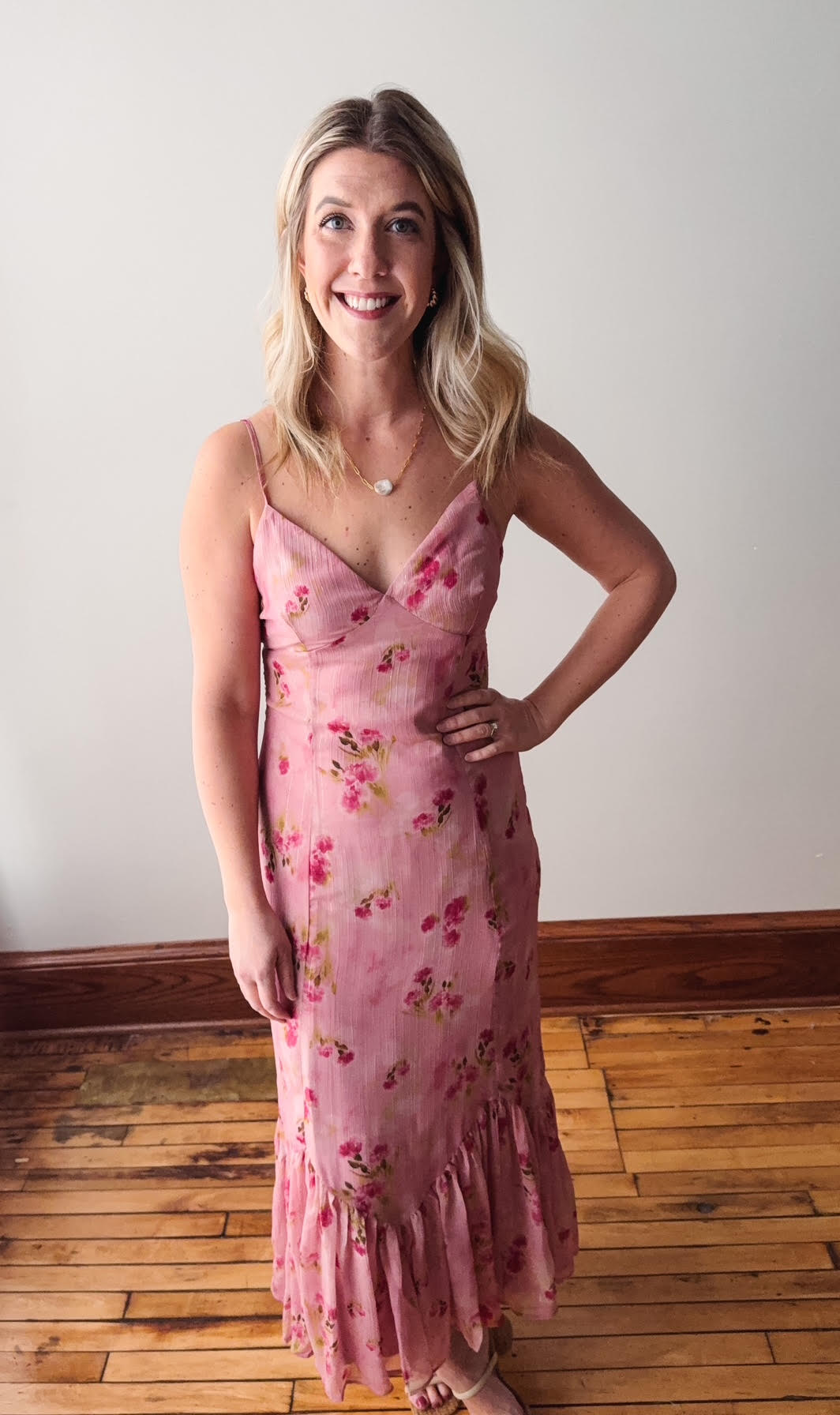 Woman wearing a pink floral dress standing on a wooden floor with a white wall background