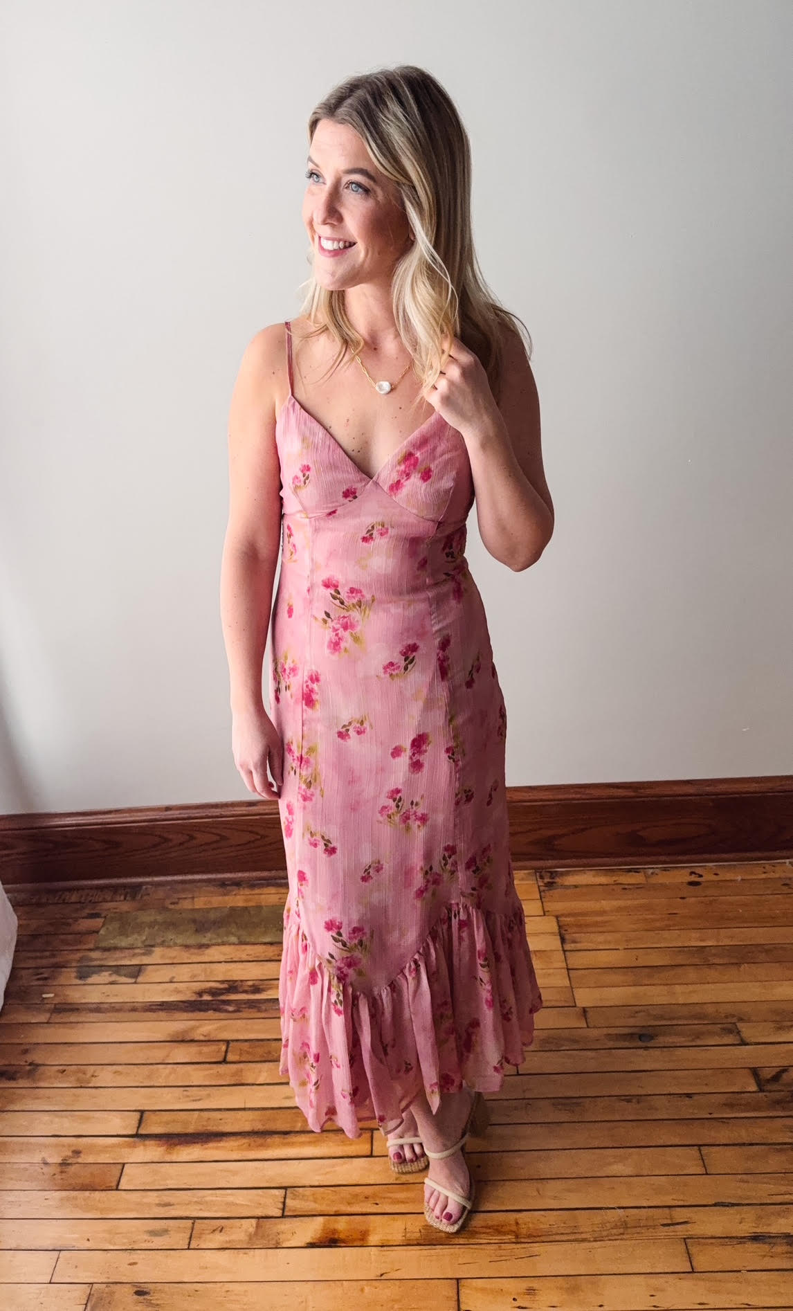 Woman wearing a pink floral dress standing on a wooden floor.
