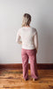 Person wearing a white sweater and pink pants standing on a wooden floor against a white wall.