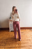 Woman taking a mirror selfie wearing a cream sweater and pink pants in a room with wooden flooring and a decorative cabinet.