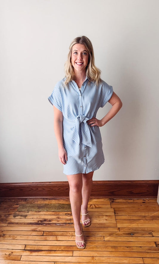 Woman wearing a blue and white striped dress standing on a wooden floor with a white wall background