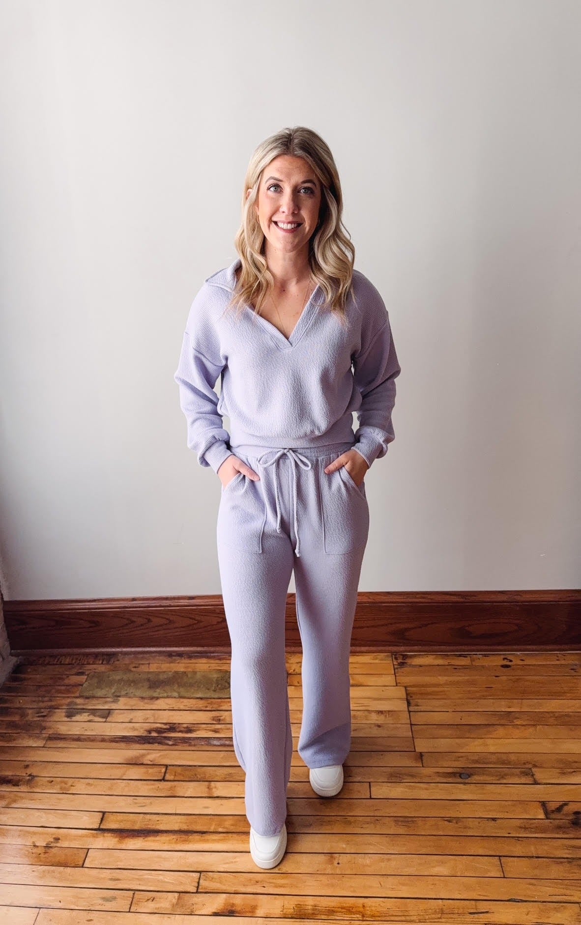 Woman wearing a light purple outfit standing on a wooden floor.