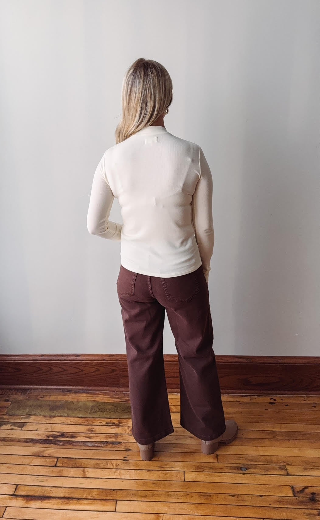 Person wearing a white shirt and maroon pants standing against a plain wall.