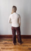 Person wearing a white shirt and maroon pants standing against a plain wall.