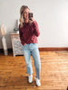 Woman taking a mirror selfie wearing a maroon sweater, light blue jeans, and white sneakers in a room with wooden flooring.