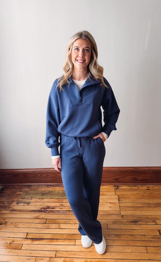 Woman wearing a blue tracksuit standing on a wooden floor with a white wall background