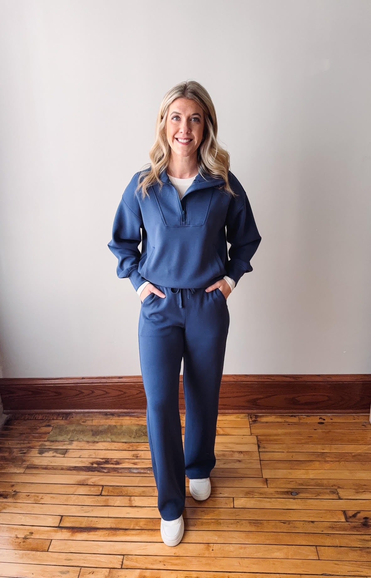 Woman wearing a blue tracksuit standing on a wooden floor with a white wall background