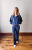 Woman wearing a blue tracksuit standing on a wooden floor with a white wall background
