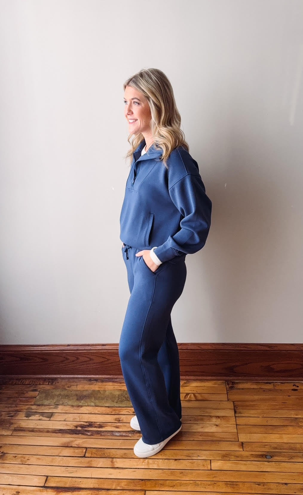 Woman wearing a blue tracksuit standing against a plain wall.