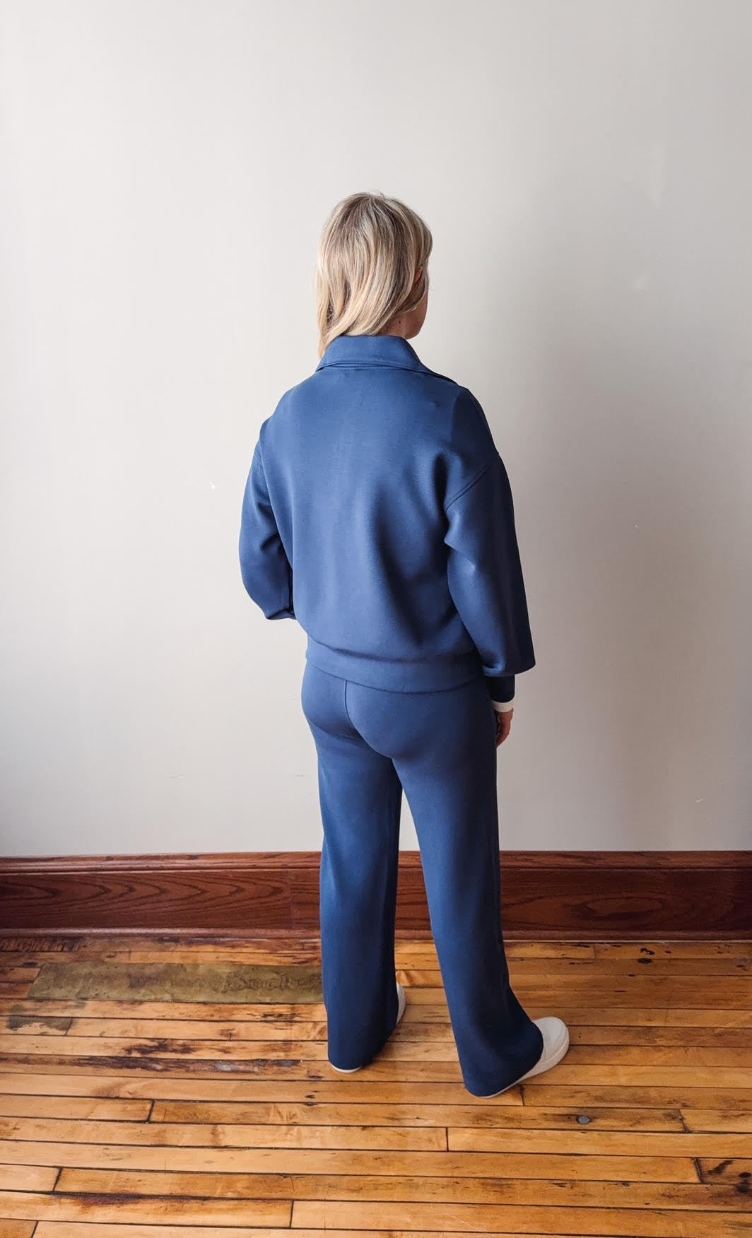 Person wearing a blue outfit standing on a wooden floor against a white wall