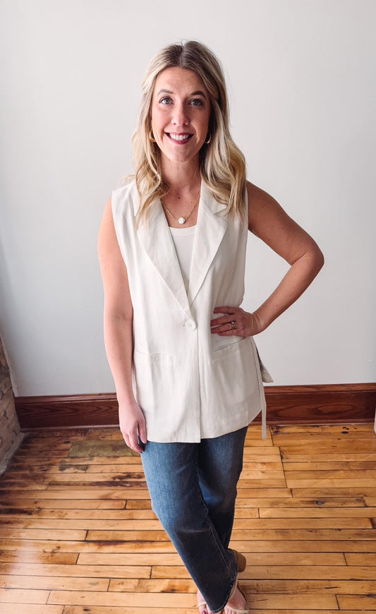 Woman wearing a white sleeveless top and blue jeans standing on a wooden floor.