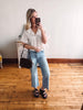 Woman taking a mirror selfie wearing a white blouse and blue jeans in a room with wooden flooring.
