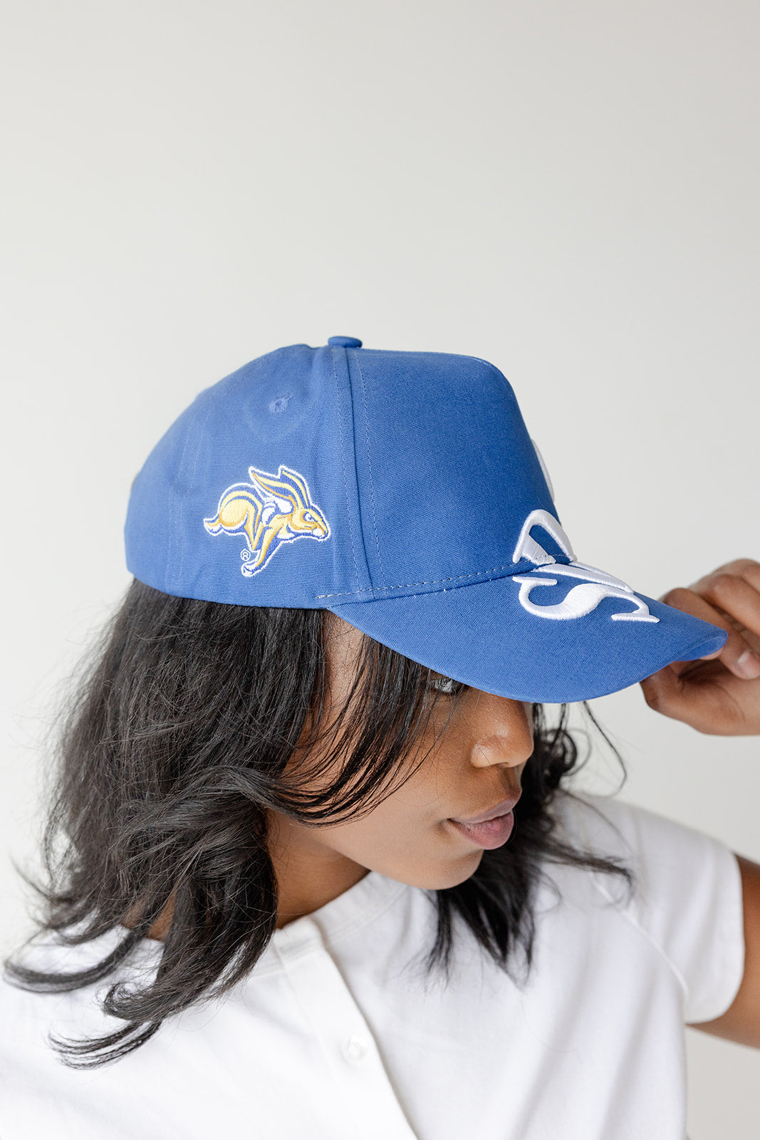 A woman wearing a royal blue baseball cap with embroidered white and yellow graphics, photographed against a plain light background.