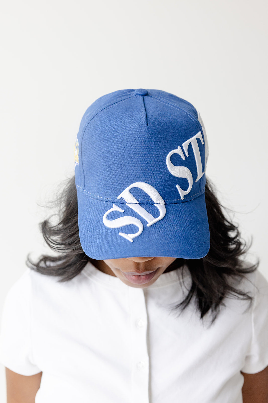 A person wearing a royal blue baseball cap with large white 'SD ST' lettering on the front, photographed against a plain light background.