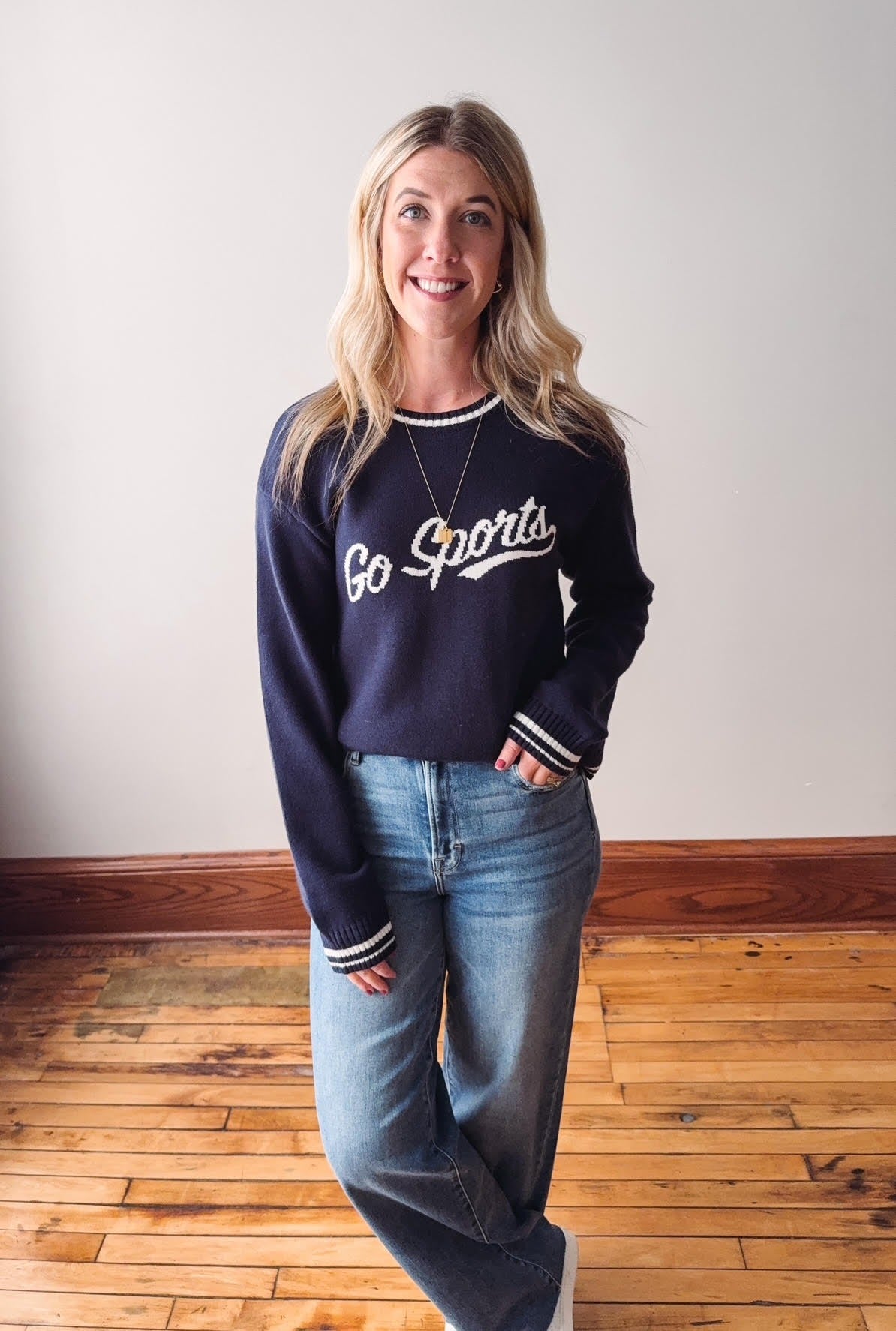 Woman wearing a navy blue 'Go Sports' sweatshirt and jeans indoors.