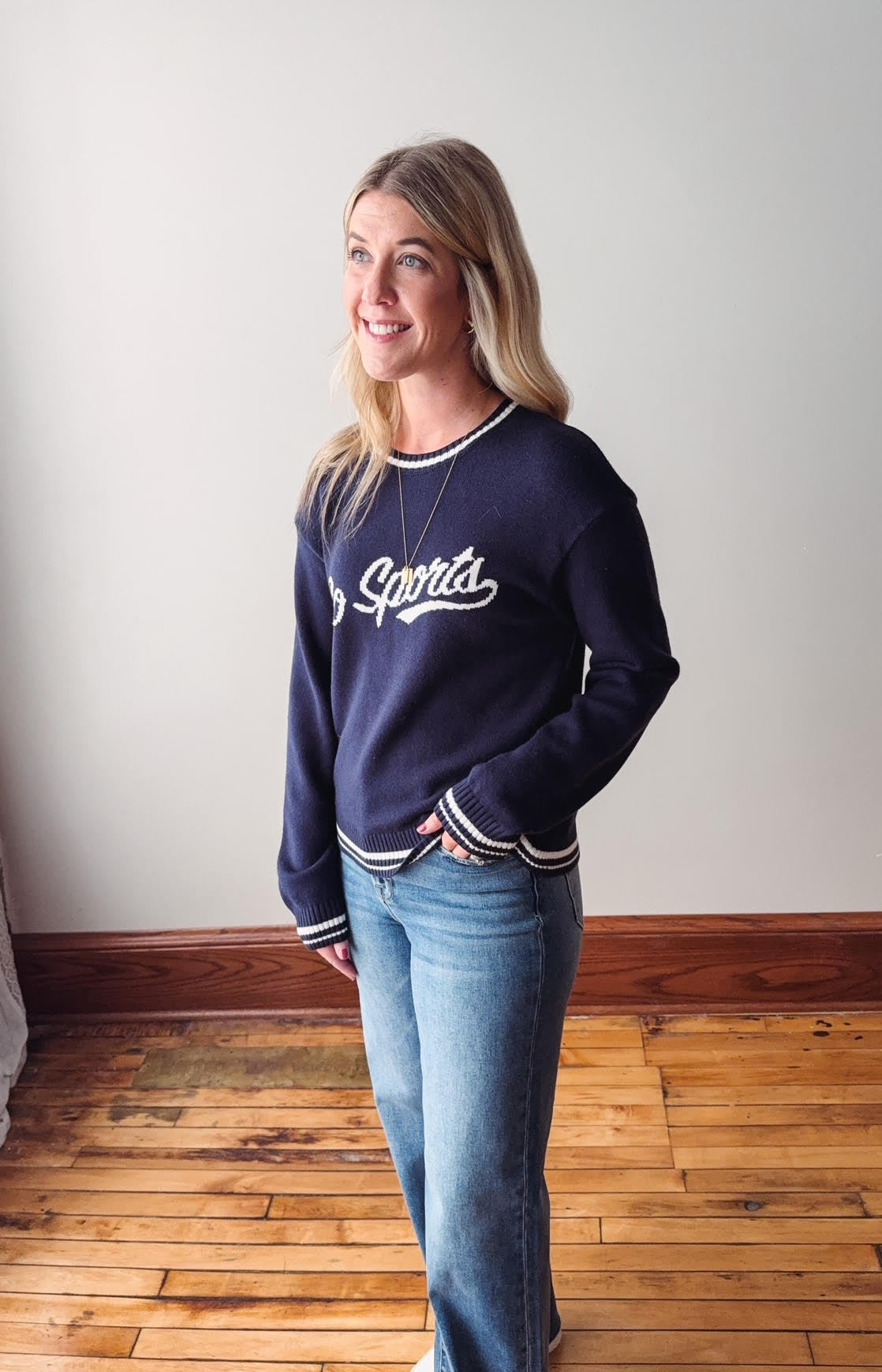 Woman wearing a navy blue sweatshirt with 'Go Sports' text, standing on a wooden floor.