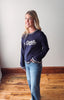 Woman wearing a navy blue sweatshirt with 'Go Sports' text, standing on a wooden floor.