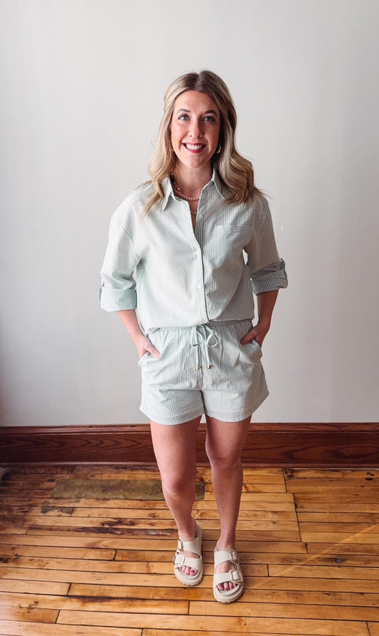 Woman wearing a light green shirt and shorts standing on a wooden floor.