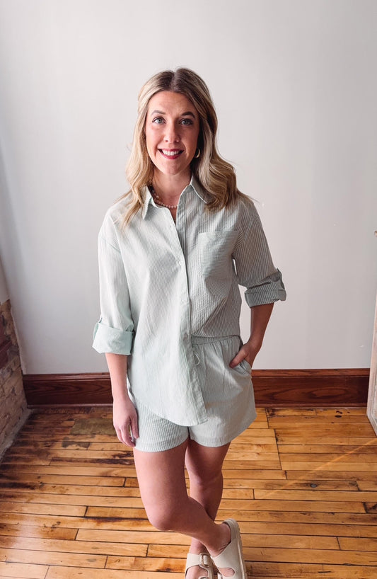 Woman wearing a light green shirt and shorts standing on a wooden floor.