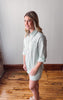 Woman wearing a light green dress standing on a wooden floor with a white wall background