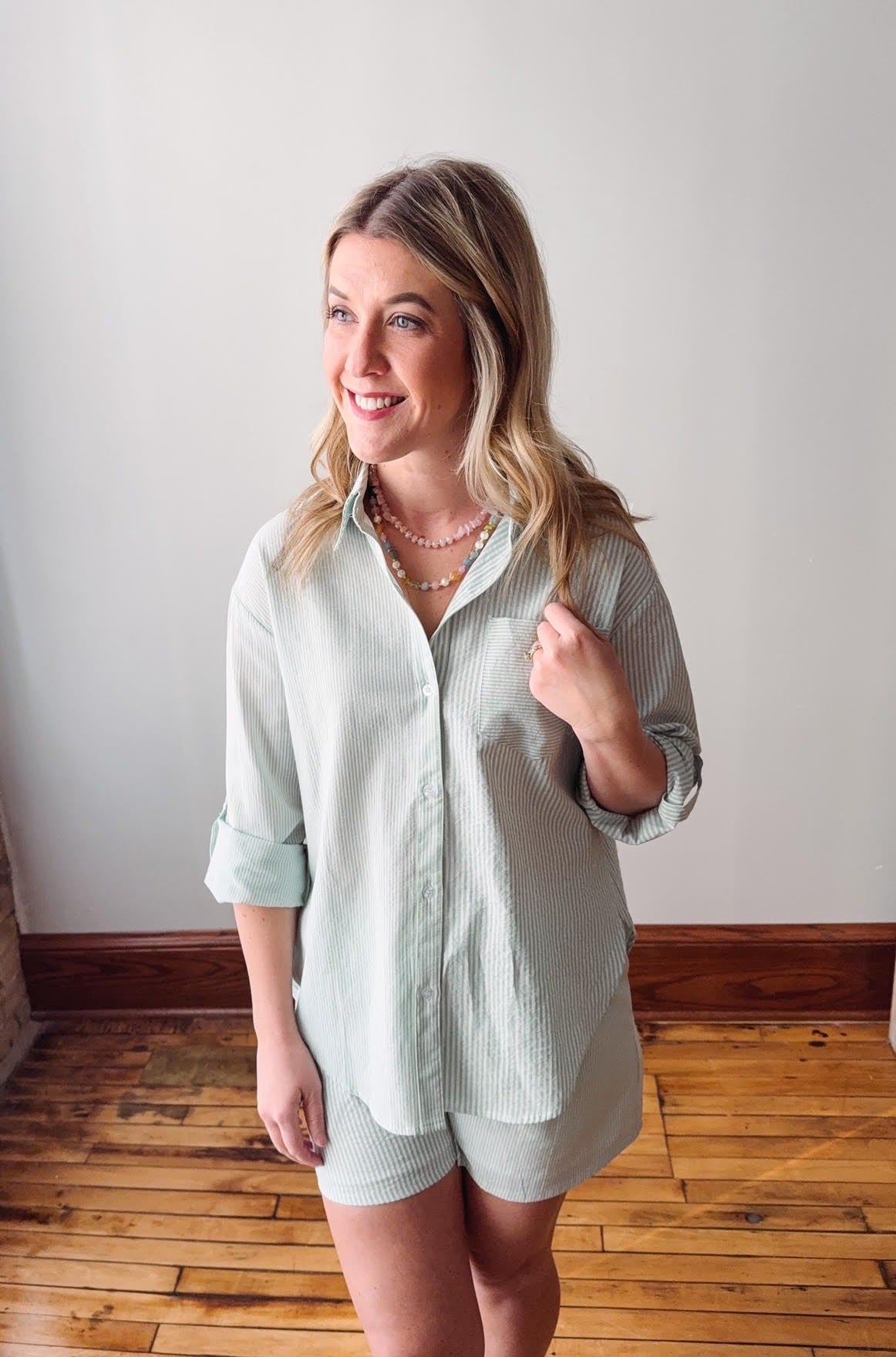 Woman wearing a light green button-up shirt and shorts standing in a room with wooden flooring.