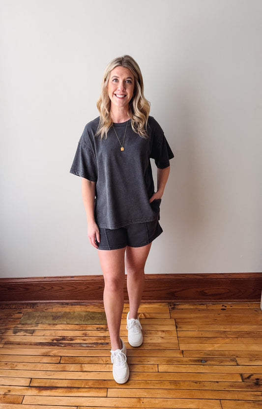Woman wearing a dark gray oversized t-shirt and shorts on a wooden floor.